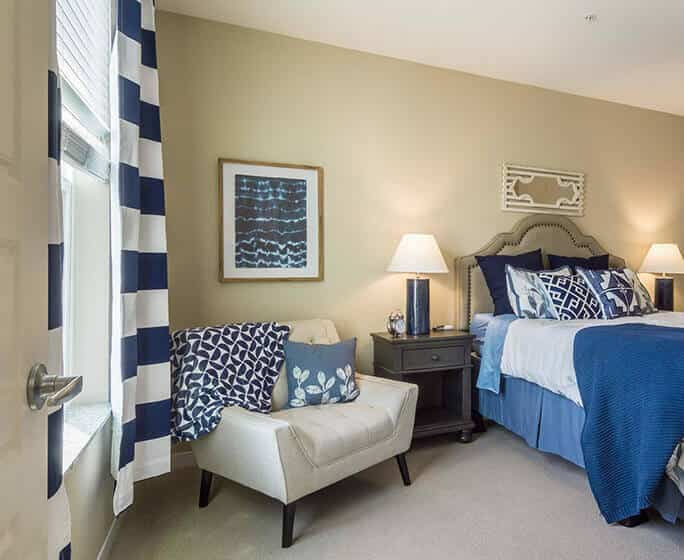 Bedroom in Park Creek model apartment with view of window on left, chair and bed in the middle and bathroom on right