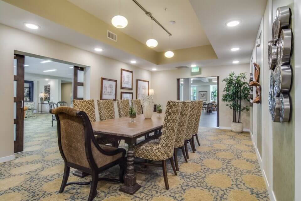 Private dining room with long dark wood table and 10 beige upholstered chairs, beige walls and level plans on walls