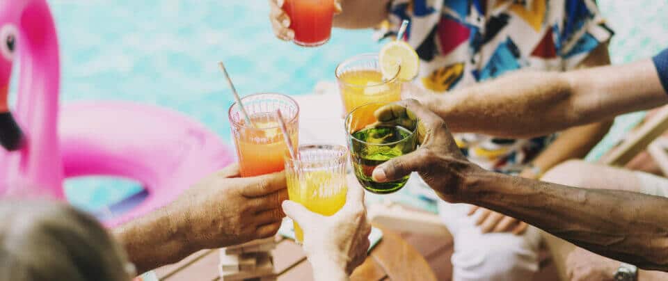 Closeup of the arms of five friends cheering with mixed drinks poolside