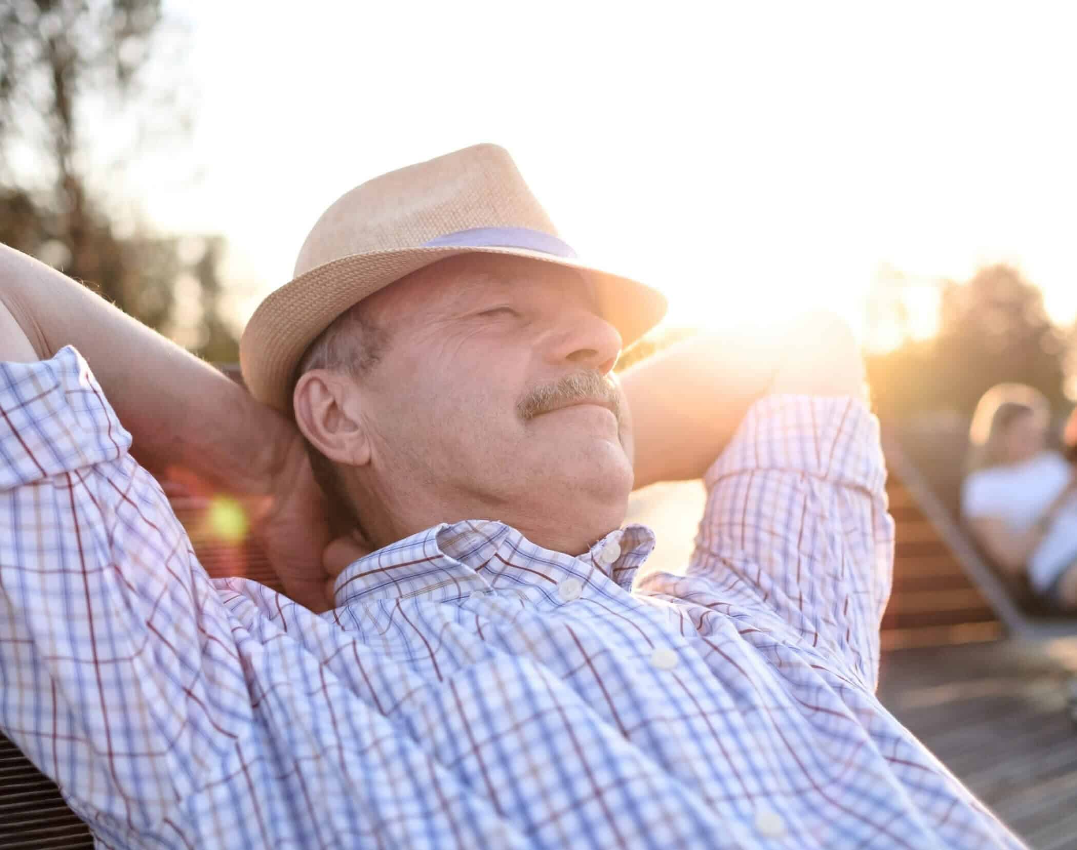 Man lays back in an outside chair with hands behind his head enjoying the sunshine.