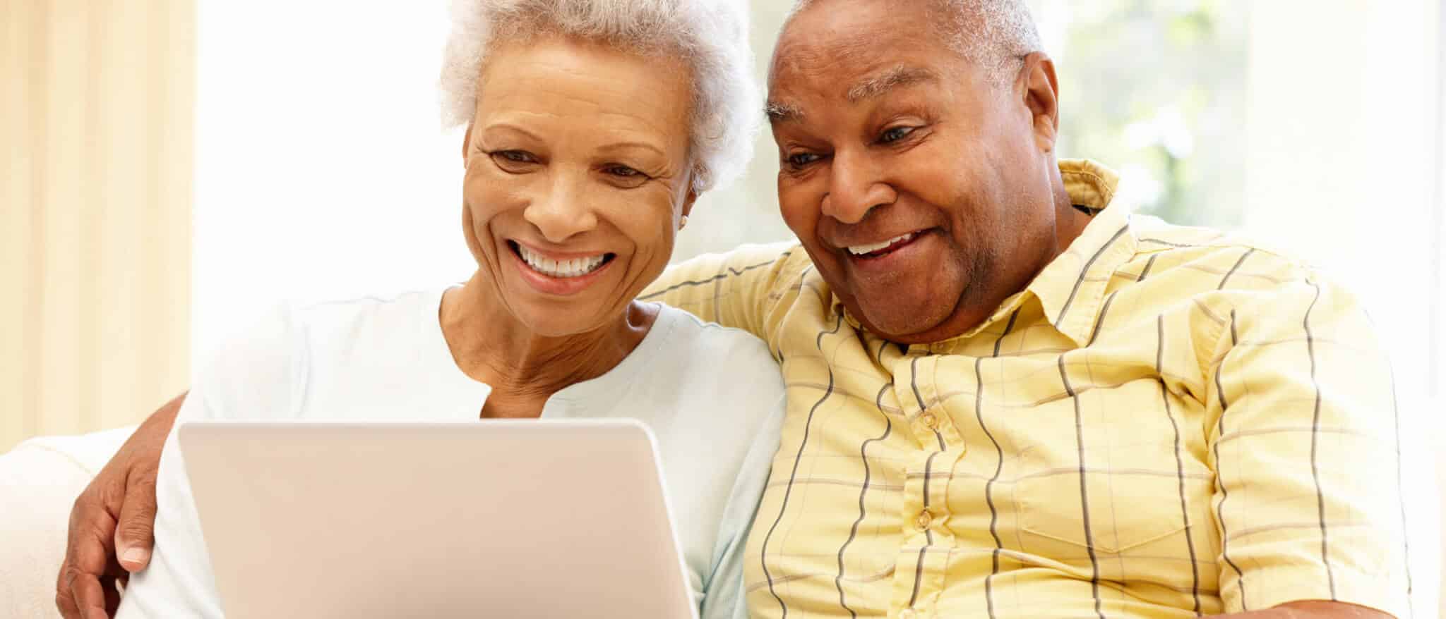 Smiling senior couple sit on couch together looking at laptop.